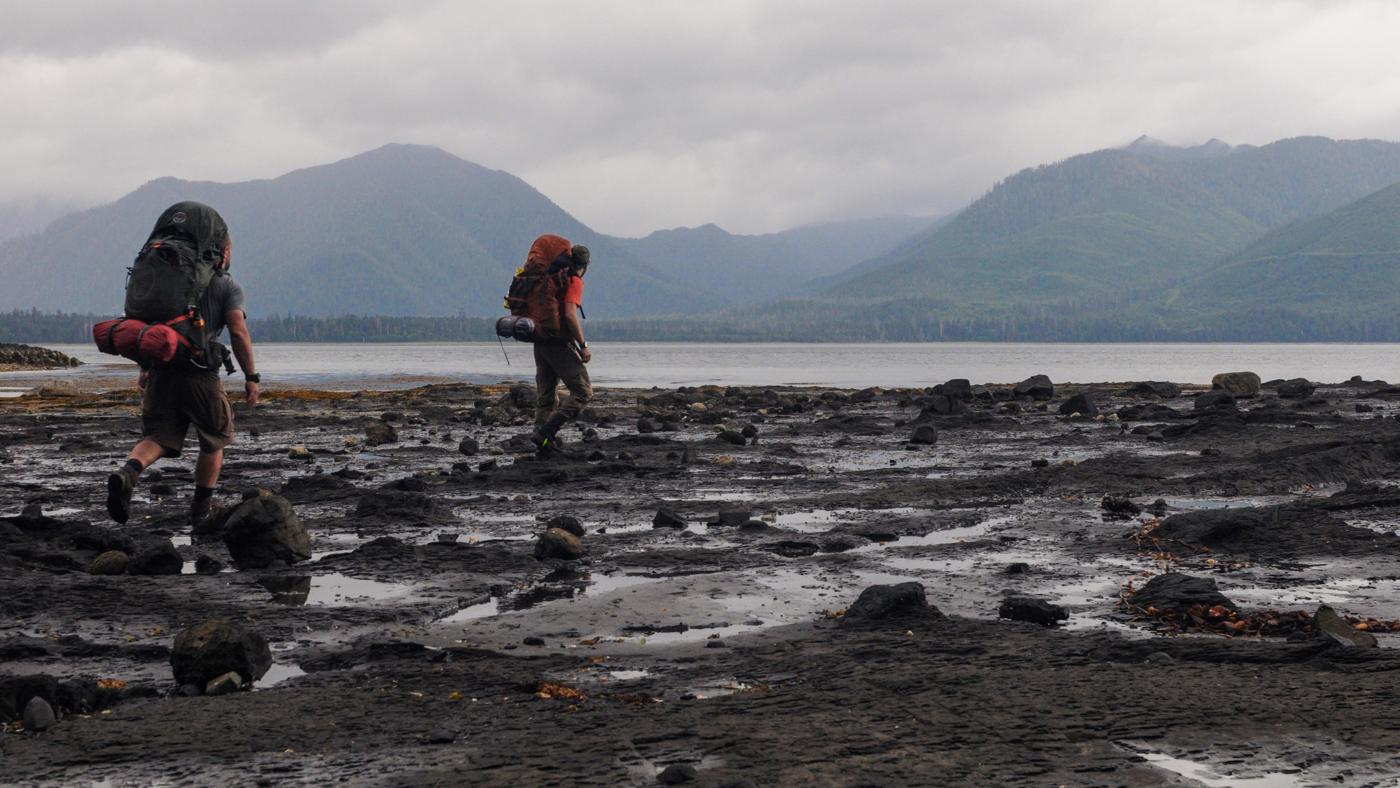 Two trekkers with heavy packs on a rocky shore